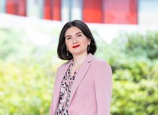Zohreh Davoudi wears a pink blazer and matching blouse in front of greenery.