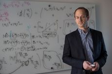 A photo of Andrew Childs standing in front of a whiteboard covered with numerous handwritten equations. 