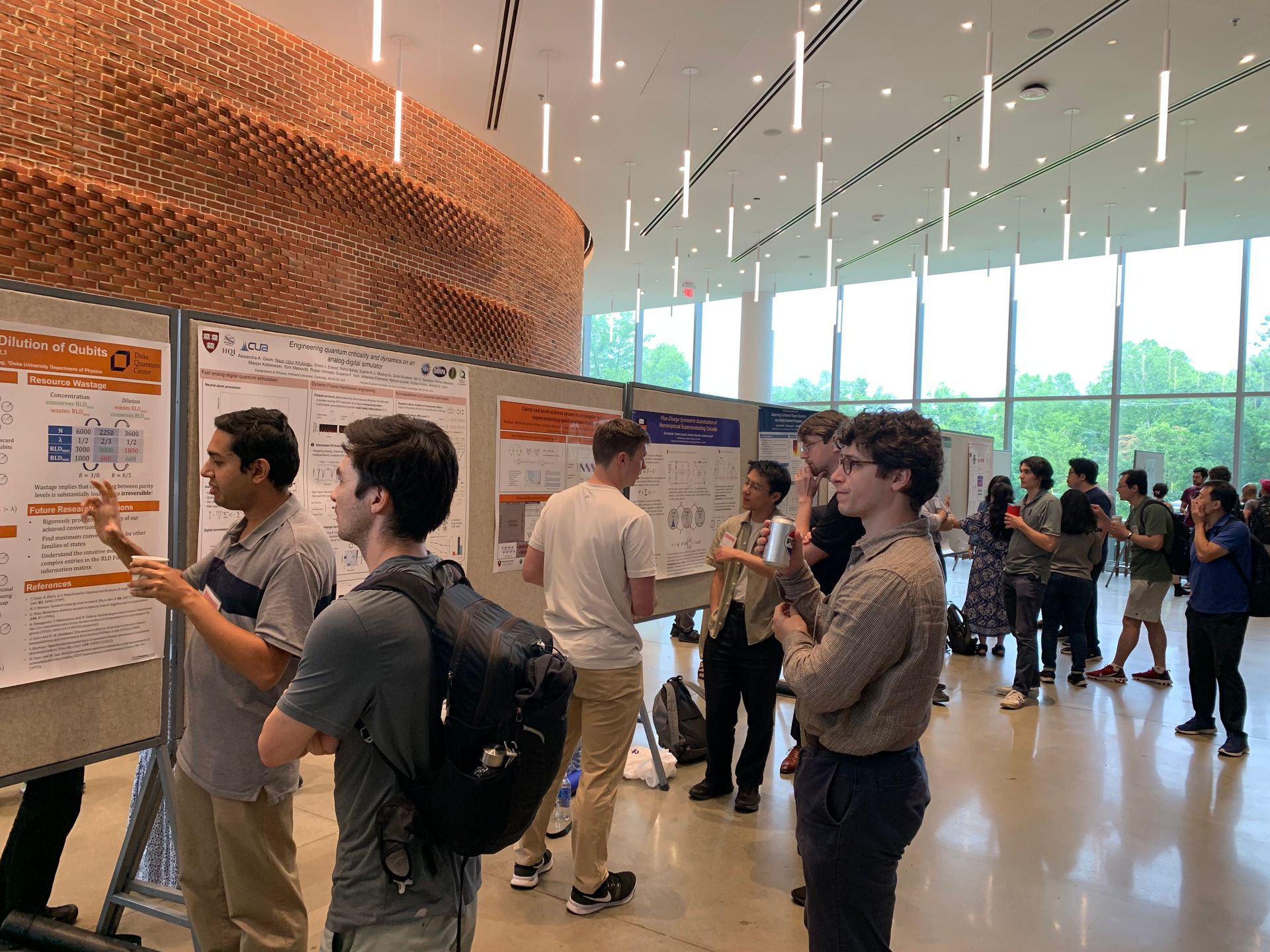 Photo of a poster session. People talk in small groups in front of a row of posters. 