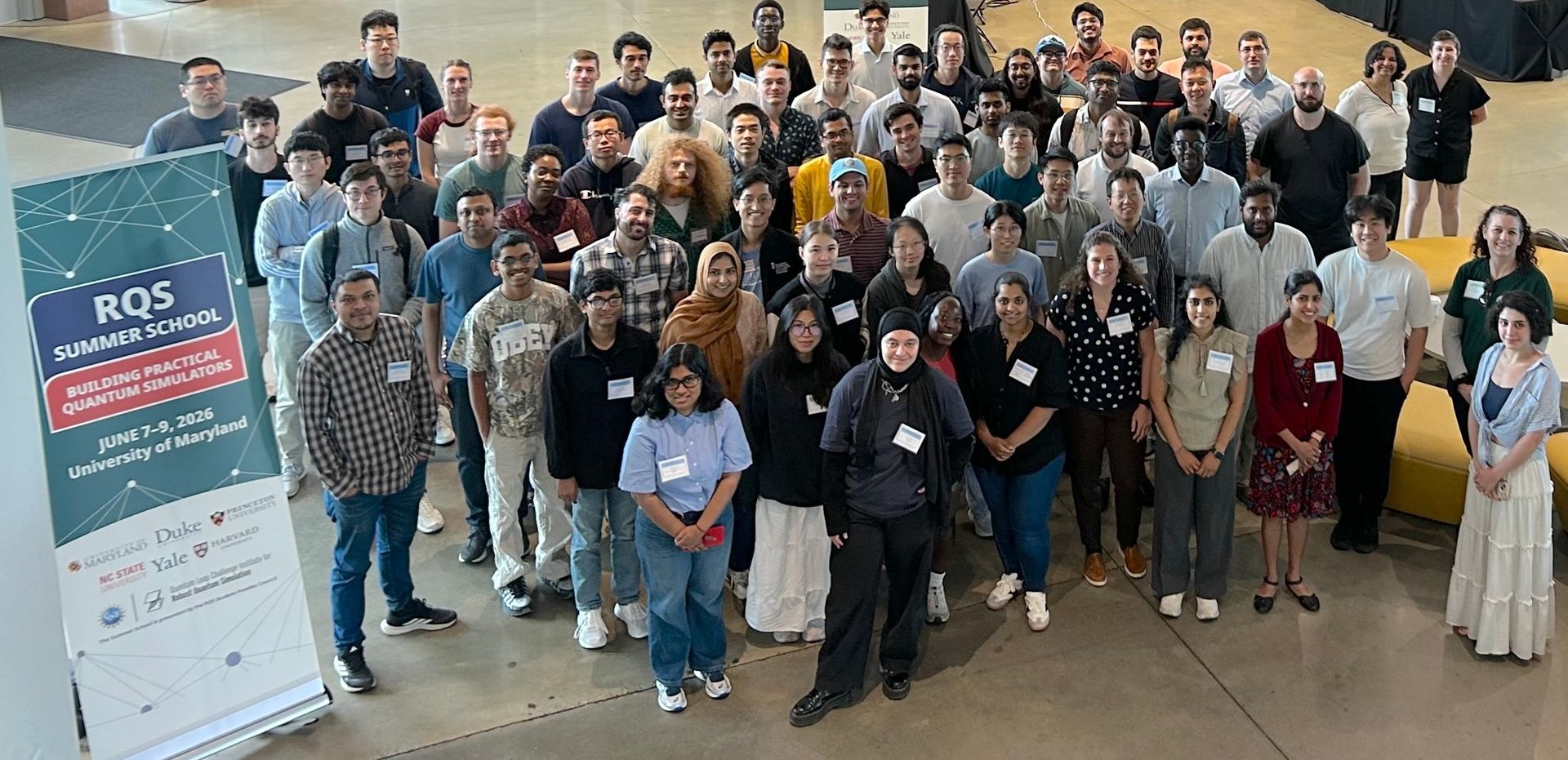 A group photo of about 60 people. A banner next to the group says "RQS Summer School: Building Practical Quantum Simulators"